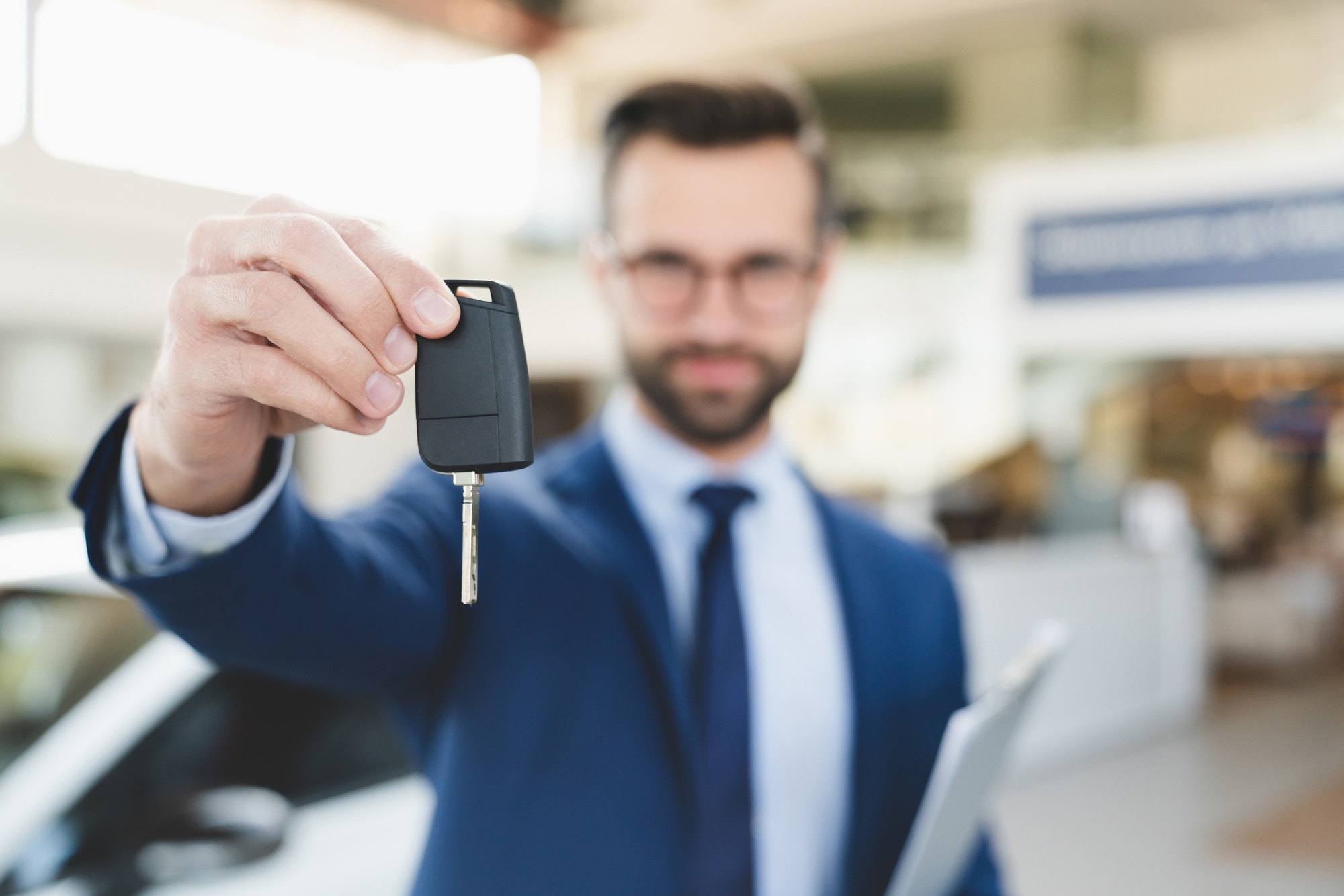 Shop assistant holding handing car keys to a client after buying new expensive car at dealer shop.